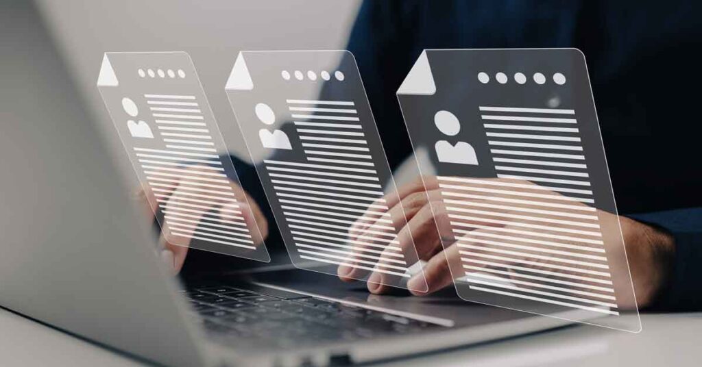 Multiple of the same resume that a man is looking at on a computer
